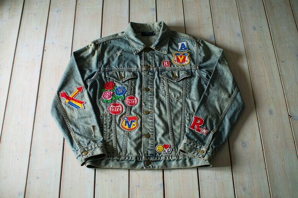 Denim jacket patches styling: vintage denim jacket covered with embroidered patches laid flat on a wooden table