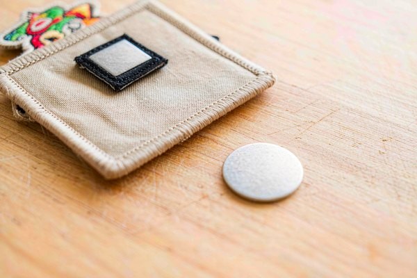 Thin magnetic strip sewn inside the backing of a custom magnetic patch, shown next to a steel plate insert for the garment side