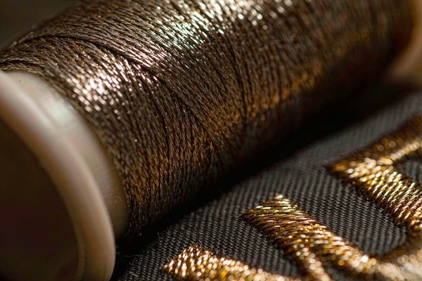 Macro detail of metallic gold thread showing the flat foil filament wound around its core, stitched into patch lettering