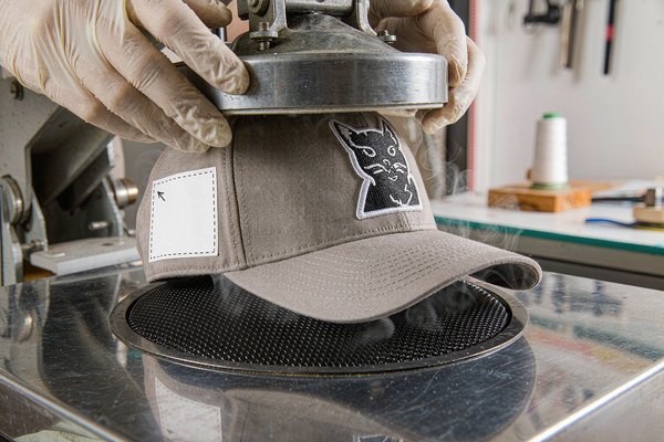 Hands heat-pressing an embroidered patch onto a cap front panel at the correct patch placement height above the brim