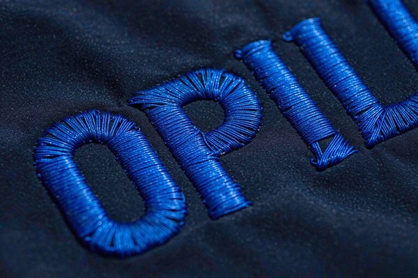 Satin stitch embroidery forming small block letters on a patch, showing tightly packed thread lines that determine patch lettering legibility